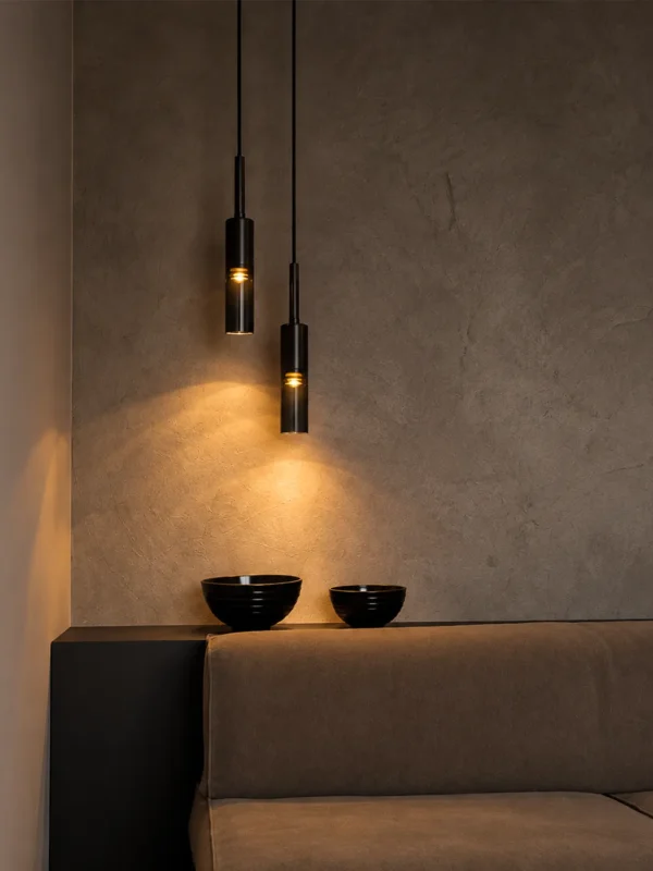 Two Abramo cylindrical pendant lights suspended at different heights above a contemporary seating area