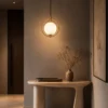 Abree decorative gold pendant light with a glowing white glass globe above a modern console table