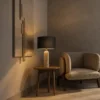 Albora Table Lamp Black Shade Albora table lamp with a black cylindrical shade and textured light-colored base beside an upholstered chair