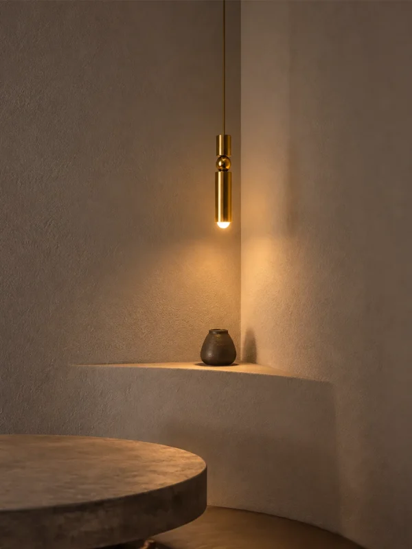 Amalea slim gold pendant light providing warm downward illumination above a minimalist interior shelf