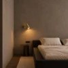 Aurelio LED Wall Spotlight Bedroom Aurelio electroplated gold wall lamp mounted above a bedside table in a minimalist bedroom