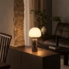 Avorio table lamp on a wooden side cabinet beside a leather armchair