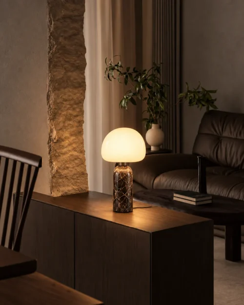 Avorio table lamp on a wooden side cabinet beside a leather armchair