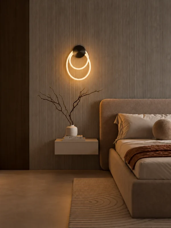 Ayla sculptural wall lamp with overlapping illuminated rings mounted beside a bed in a modern bedroom