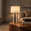Lithos Table Lamp Living Room Lithos table lamp with white drum shade on a wooden side table beside an upholstered sofa