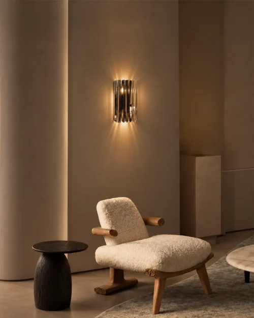Martina chrome wall lamp providing warm accent lighting above an upholstered lounge chair