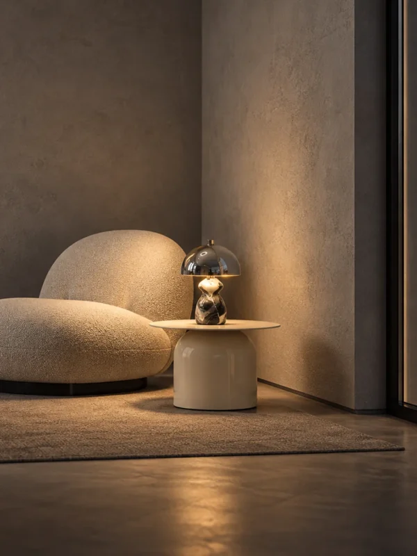 Nero sculptural table lamp on a round side table beside a curved upholstered chair