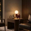 Noelle Table Lamp Contemporary Living Room Noelle table lamp with a glowing white glass globe and maroon curved base on a wooden side table