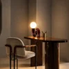 Noelle Table Lamp Modern Interior Noelle maroon sculptural table lamp displayed on a wooden desk beside an upholstered chair