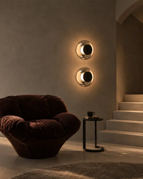 Two Orbe circular wall lamps mounted vertically beside a lounge chair in a modern interior