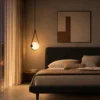 Orbit geometric pendant light with a glowing white globe beside a bed in a contemporary bedroom